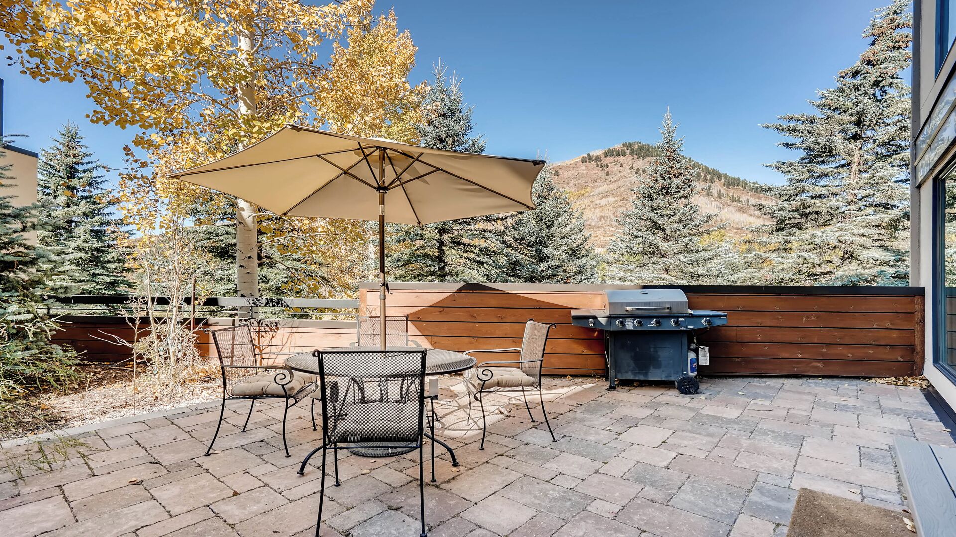 Un patio con mesa y sillas, una parrilla, y vistas a árboles y una montaña.
