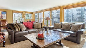 Een ruime woonkamer met leren banken, een houten salontafel en grote ramen met uitzicht op een besneeuwd landschap.