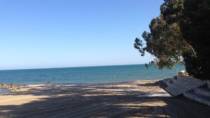 Una spiaggia sabbiosa con vista libera sul mare, qualche panchina e una scala in pietra che scende verso l'acqua.
