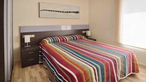 Una camera da letto con un letto, un comodino, un cassetto, una lampada e un'opera d'arte appesa al muro.