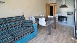 Un ambiente compatto con divano, tavolo da pranzo, sedie e angolo cottura.