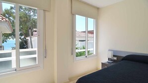 Una camera da letto con un letto, un comodino e una finestra vista mare e alberi.