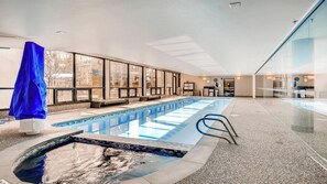 Una piscina interior con vistas despejadas al exterior gracias a grandes ventanales, un área de descanso con asientos y una recepción.