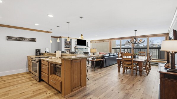 Una cocina moderna con una isla central, armarios de madera y un comedor con un ventanal grande.