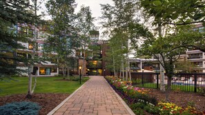 A pathway leading to a building with a modern design, surrounded by trees and a flower bed. - Spacious 2BR • Open Concept • Remodeled Kitchen & Baths | Flexible Sleeping (Vail)