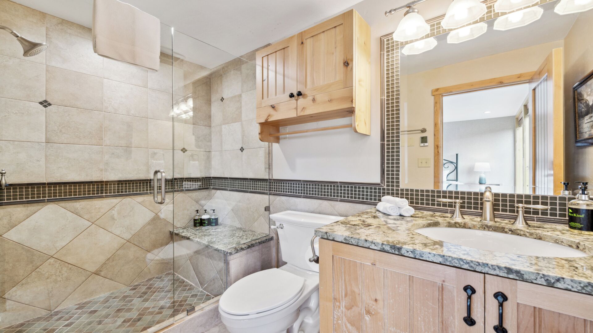 Un bagno moderno con box doccia in vetro, un WC, un lavabo con piano in marmo e mobili contenitori in legno.