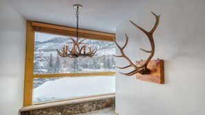 A room with a large window overlooking a snowy mountain landscape, a wooden beam ceiling, and a mounted antler decoration. - Spacious 3BR Mountain Lodge • Stone Fireplace • Vaulted Ceilings & Mountain View (Vail)