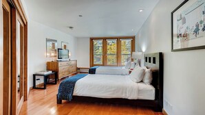 A bedroom with two beds, a dresser, a TV, and a balcony with a view of trees.