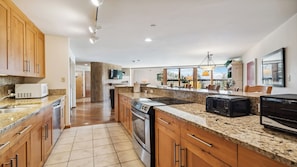 A modern kitchen with granite countertops, wooden cabinets, a built-in oven, and a large island with a toaster.