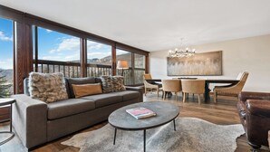 Ein modernes Wohnzimmer mit Sofa, Couchtisch und Essbereich, mit großen Fenstern und Blick auf die Berge.