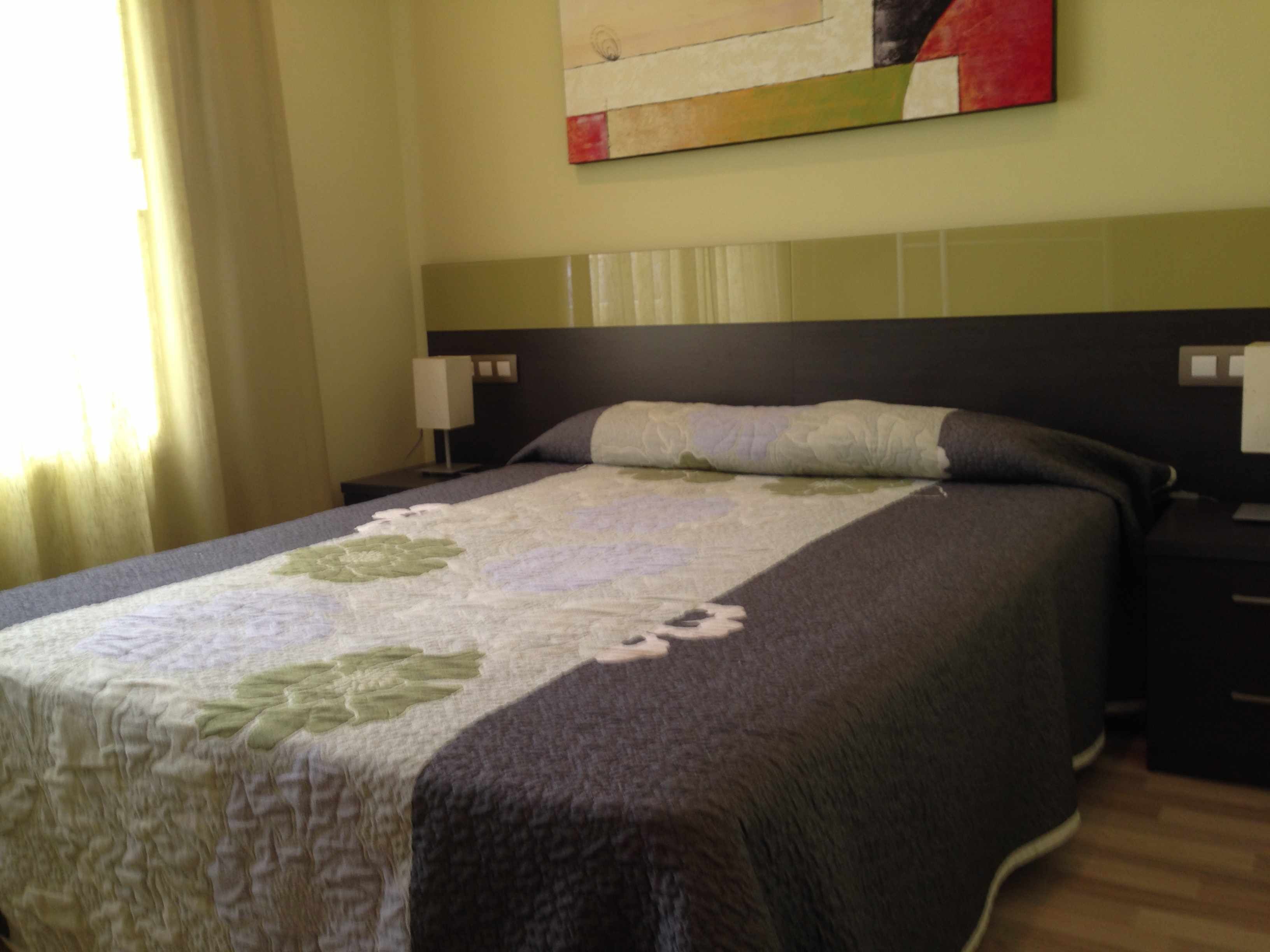 A neatly made bed with a floral-patterned bedspread, a dark headboard, and two bedside lamps.