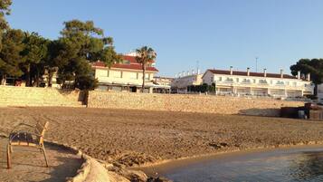 Un hotel junto a la costa con varios balcones, una pared de piedra y una playa de arena.