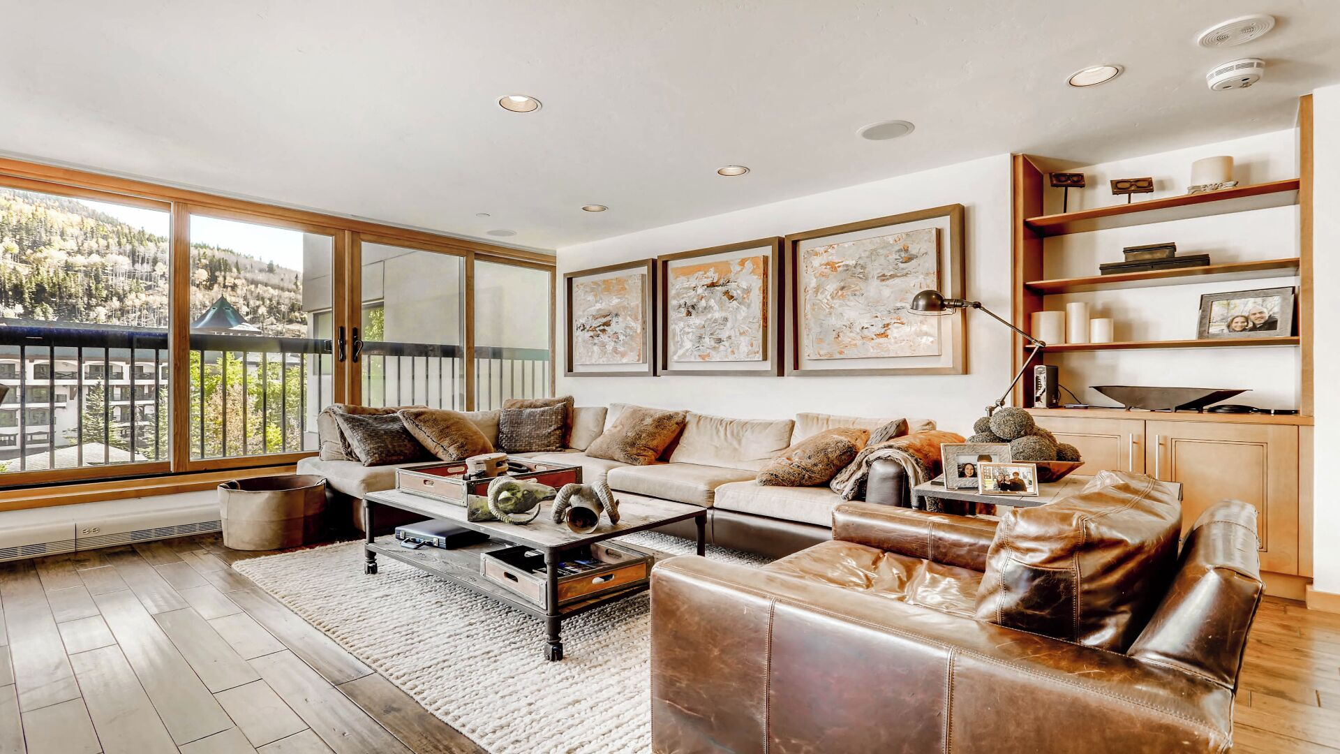 A spacious living room with a large window, a sofa, a coffee table, and a bookshelf.