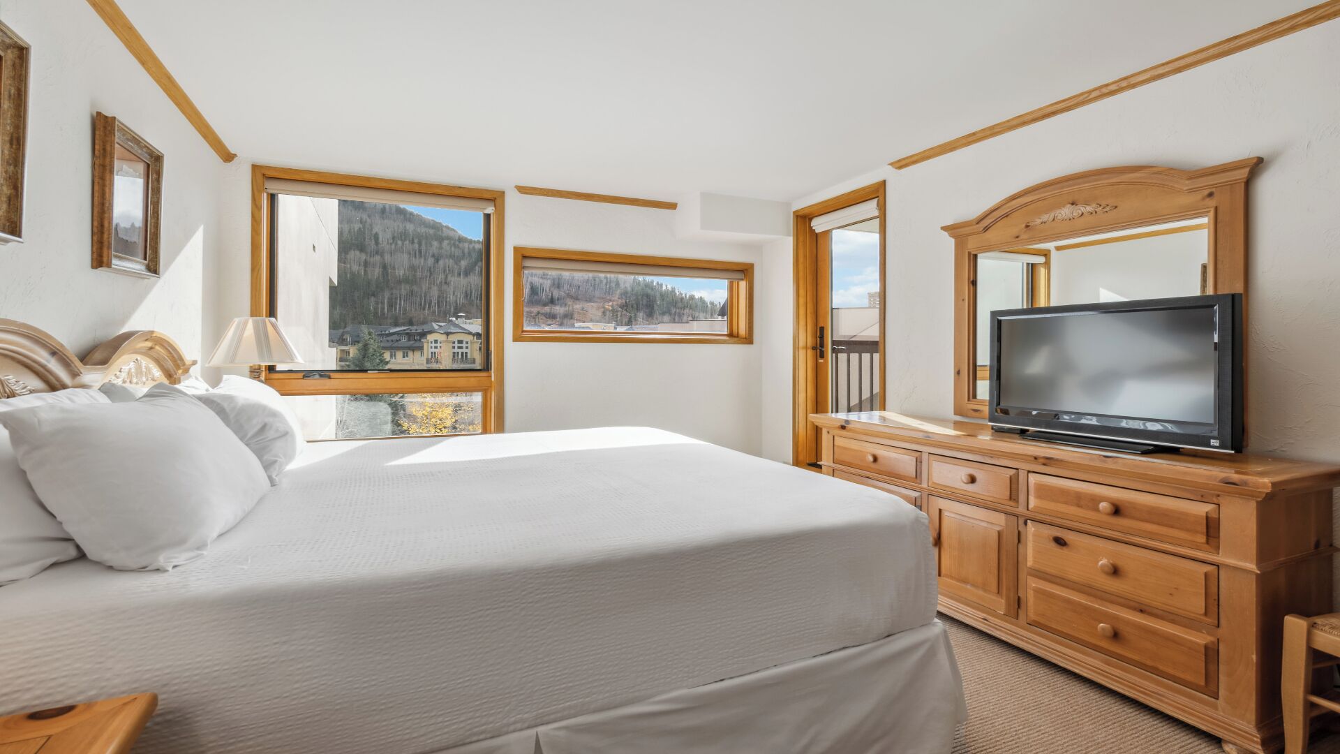 Ein Schlafzimmer mit Bett, einem Fernseher auf einer Holzkommode und großen Fenstern mit Blick auf die Berge.
