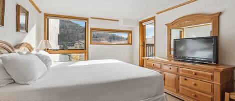Ein Schlafzimmer mit Bett, einem Fernseher auf einer Holzkommode und großen Fenstern mit Blick auf die Berge.