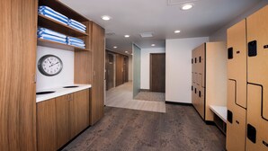 A hotel corridor with wooden lockers, a clock, and a tiled floor.
