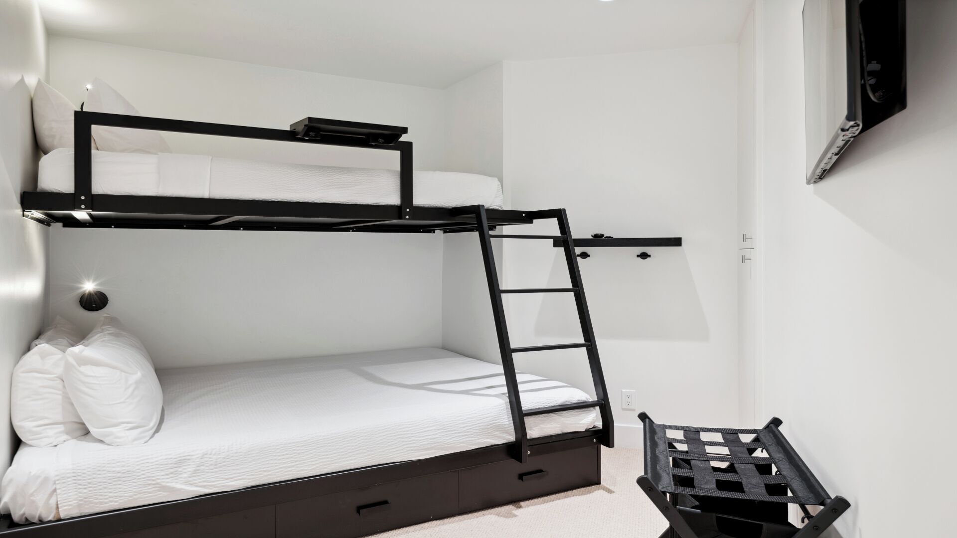 Una cama litera con escalera, un escritorio pequeño y una silla en una habitación con paredes blancas.