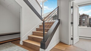Eine moderne Treppe mit Holzdielen und Metallgeländern, die zu einem Balkon mit Stadtblick führt.