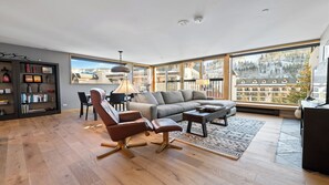 A spacious living room with a large window, a sofa, a coffee table, and a bookshelf.