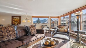 A cozy living room with a sofa, armchairs, a coffee table, and a view of mountains through large windows.