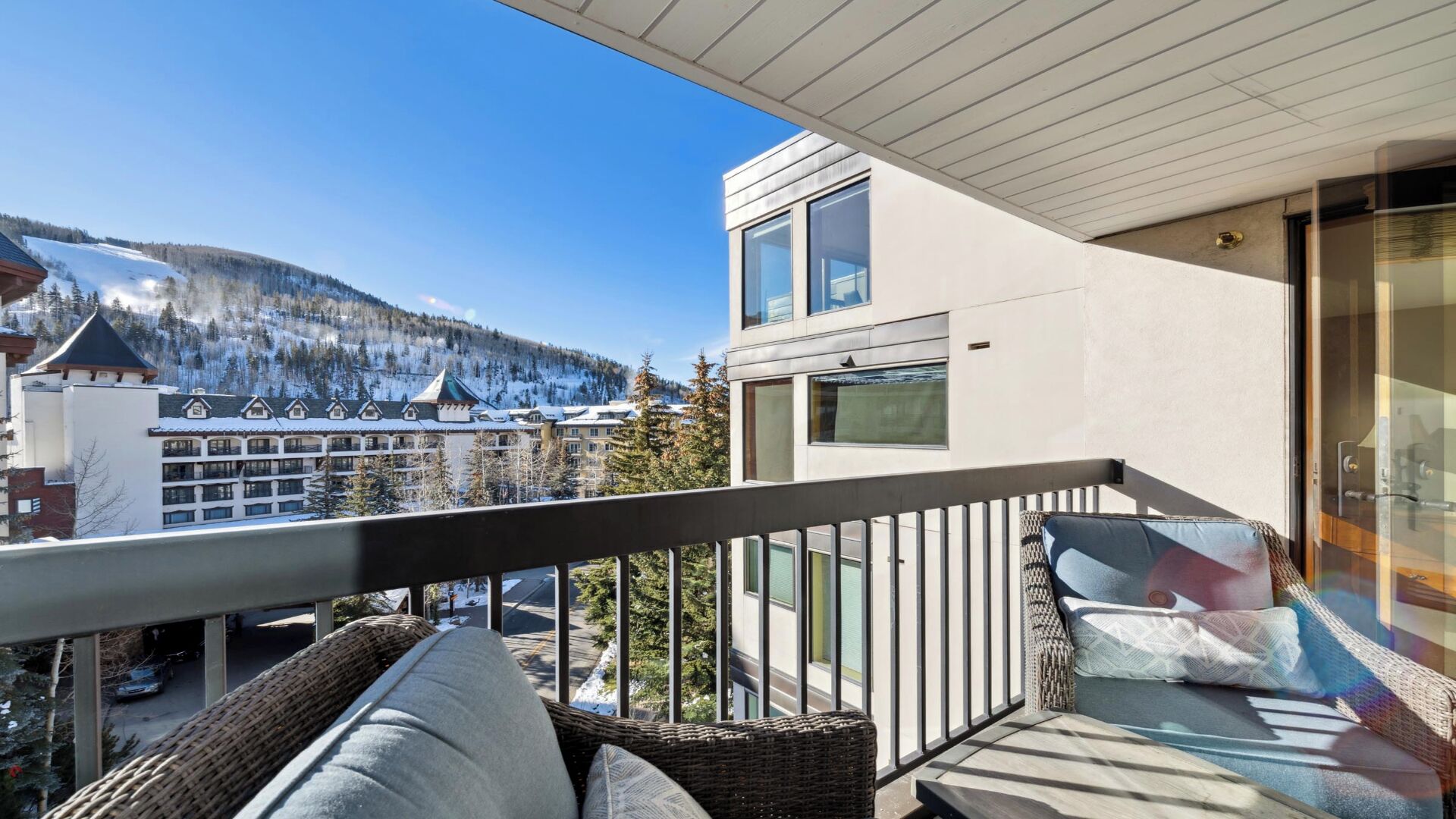 Un balcon agrémenté de meubles en osier, une vue sur une montagne et un bâtiment au design moderne.