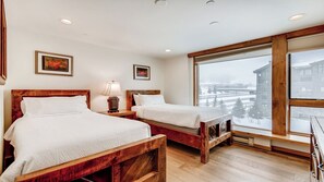 A room with two wooden beds, a large window with a view of a snowy landscape, and a framed picture on the wall.