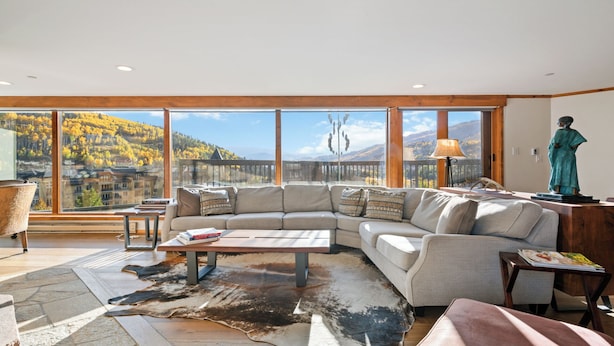Ein geräumiges Wohnzimmer mit einer großen Eckcouch, einem Couchtisch und Blick auf eine Berglandschaft durch große Fenster.