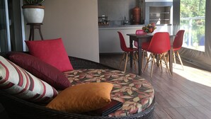 A cozy living area with a sofa, red and patterned cushions, a dining table with red chairs, a potted plant, and a kitchen area with a grill. - Brotas Shangri-lá with 3 suites, pool and stunning views! (Caju)