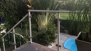 A poolside area with a metal railing, a blue pool, and lush greenery including banana leaves and palm trees. - Brotas Shangri-lá with 3 suites, pool and stunning views! (Caju)