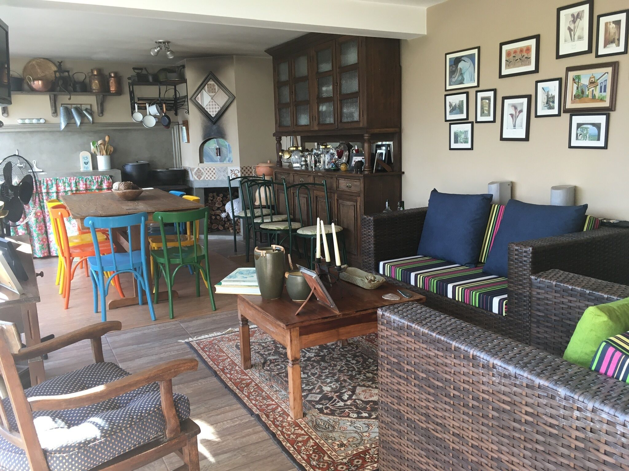 Uma sala de estar aconchegante com um sofá de vime, cadeiras coloridas, uma mesa de jantar e uma área de cozinha com panelas de cobre.