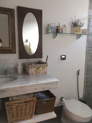 A bathroom with a marble sink, a large mirror, wicker baskets, a toilet, and a glass shower enclosure. - Brotas Shangri-lá with 3 suites, pool and stunning views! (Caju)
