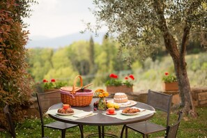 Mesa redonda al aire libre con una cesta de mimbre, un pastel y platos de comida.