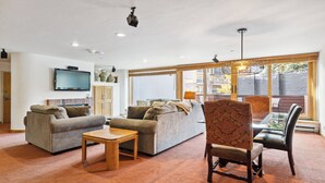 A living room with a sofa set, a coffee table, a TV mounted on the wall, and a large window with a view of the outside. - Beautiful 2BR Retreat • Comfortable & Convenient Stay (Vail)