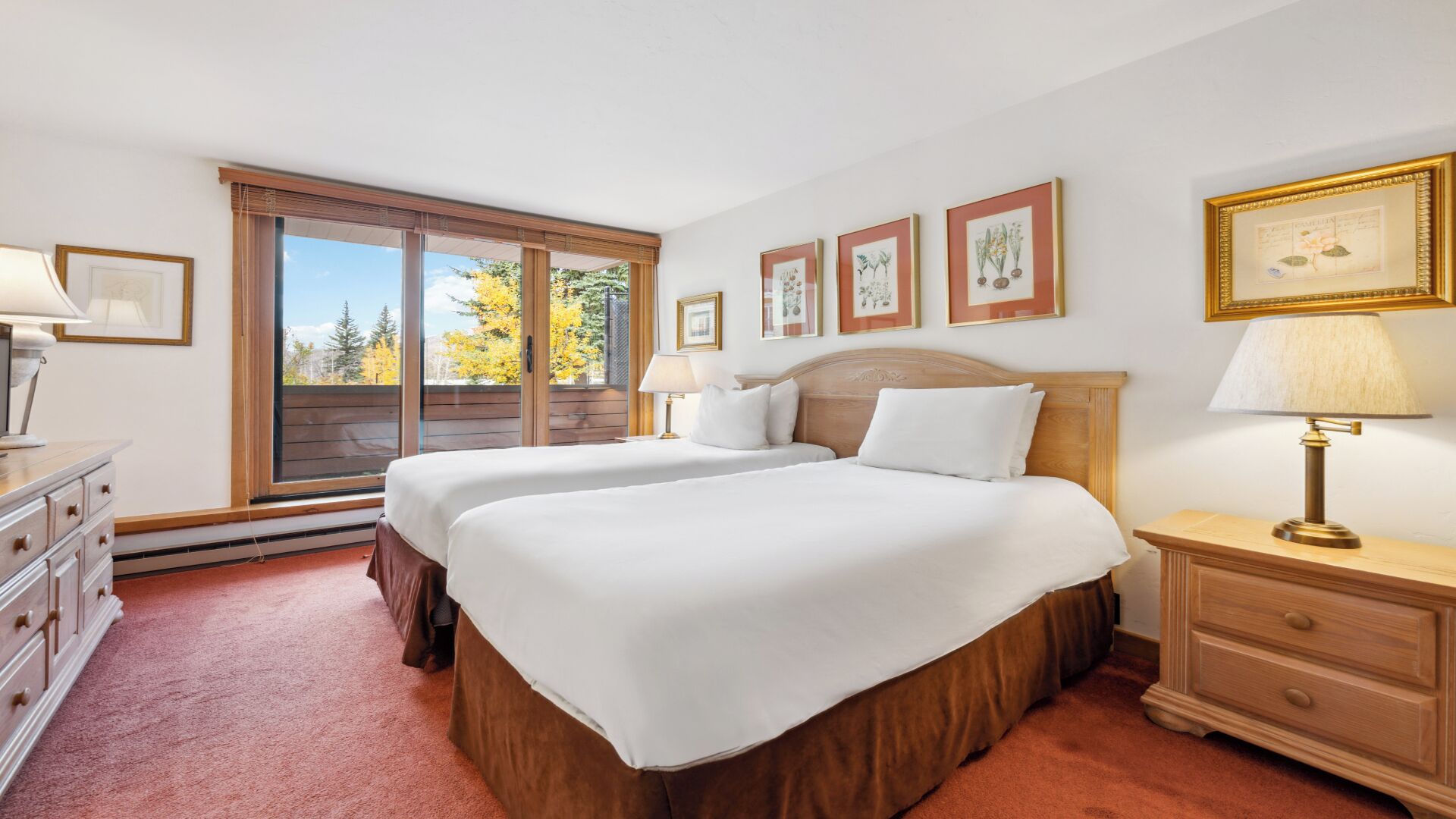 A hotel room with two beds, a dresser, a nightstand, and a window with a view of trees.