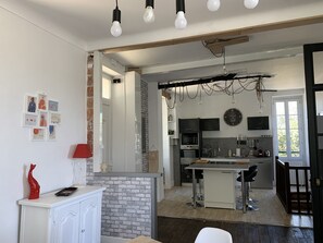 Una cocina moderna con una isla central, un comedor con una lámpara roja y una pared de ladrillo.