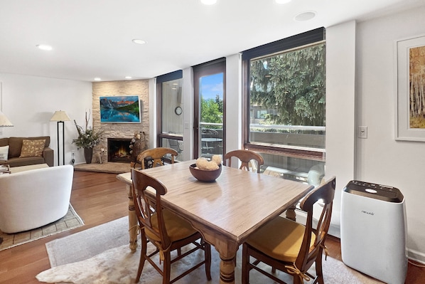 A modern living room with a wooden dining table, chairs, a sofa, and a fireplace.