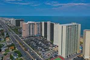 A high-rise hotel with multiple floors, a parking lot, and a view of the ocean.