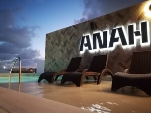 Ein Poolbereich mit Liegestühlen und einer Wand mit leuchtenden Buchstaben 'ANAH'.