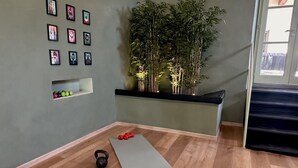 Een kamer met een grijze yogamat, kettlebells en gewichten op de vloer. Tegen de muur staat een plank met groene ballen en een bamboe plant.