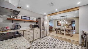 Cocina moderna con microondas integrado, refrigerador y cafetera. Se ve un área de comedor con una mesa y sillas a través de un acceso abierto.