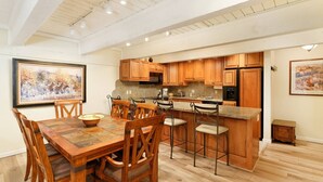 A spacious kitchen with wooden cabinets, a granite countertop, and a dining area with a wooden table and chairs. - Cottonwoods by iTrip Aspen Snowmass (Aspen)