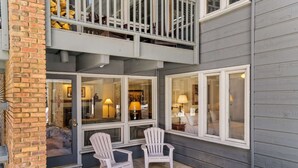 A two-story building with a balcony, a covered patio area with two Adirondack chairs, and a view into the interior through large windows. - Cottonwoods by iTrip Aspen Snowmass (Aspen)