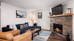 A living room with a stone fireplace, a large TV mounted above it, a sofa, a coffee table, and a rug.