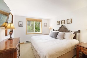 Ein Schlafzimmer mit einem großen Bett, einem Holzkopfteil, Nachttischen, einer Lampe und gerahmten Bildern an der Wand.