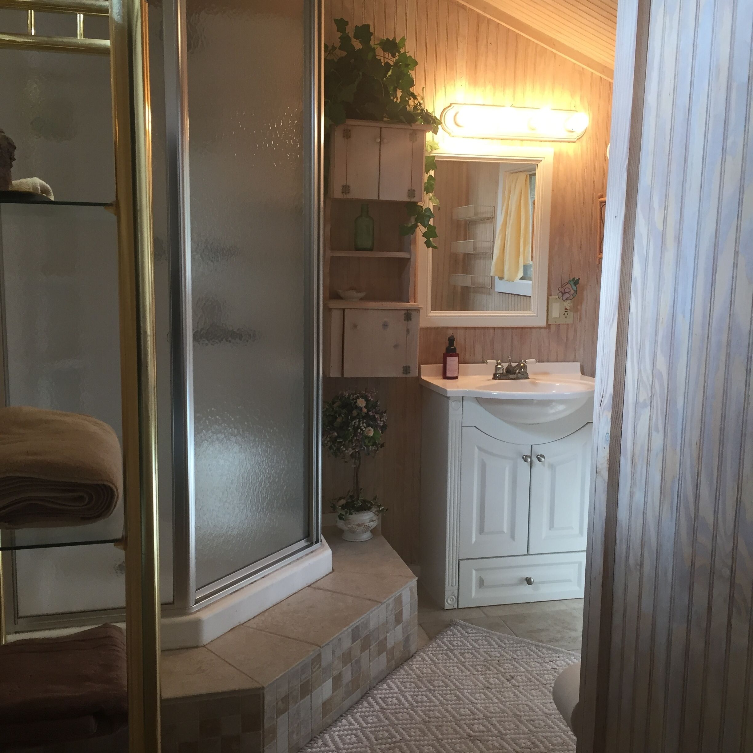 Un bagno con box doccia in vetro, un lavandino bianco con specchio sopra e pavimento piastrellato.
