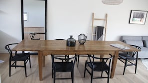 Un coin repas avec une table en bois, des chaises noires, un vase et une échelle appuyée contre le mur.