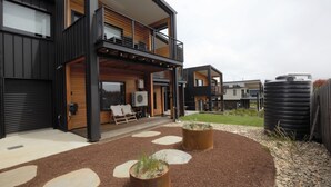 Una casa moderna de dos pisos con balcón, patio cubierto y jardín con piedras decorativas.