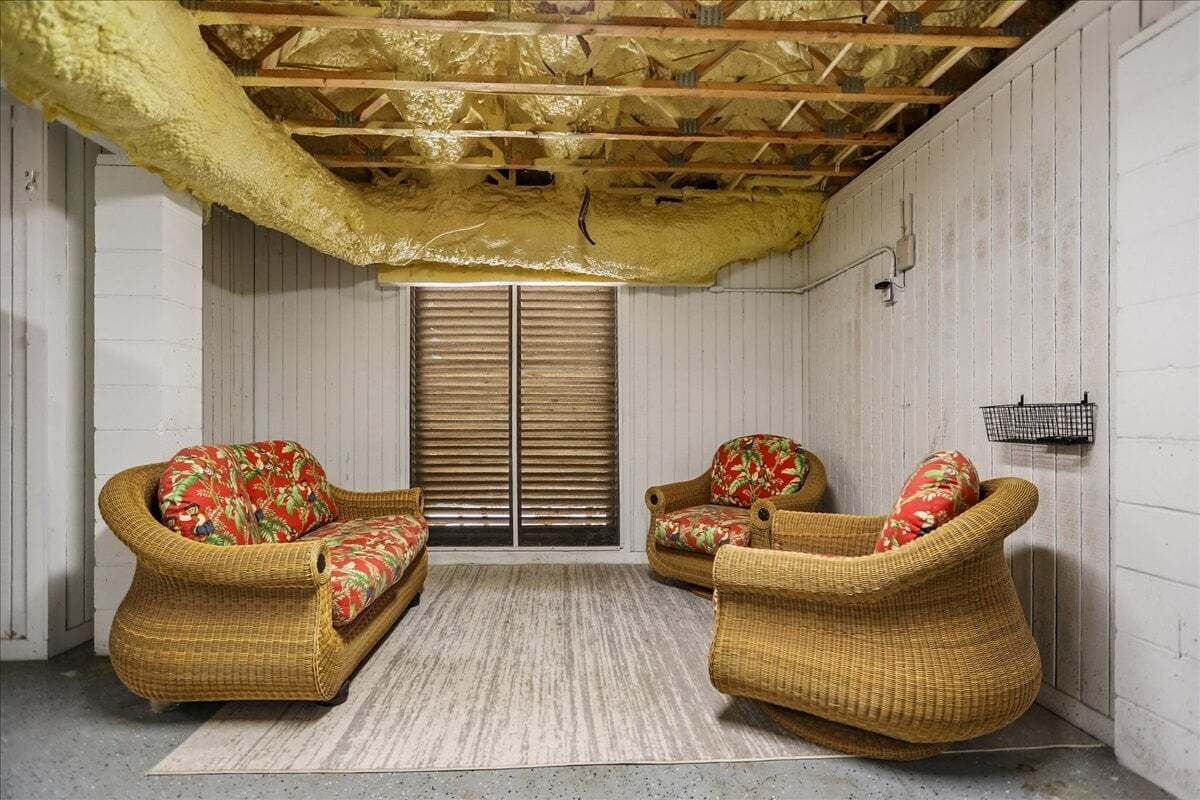 A room with two wicker chairs, a patterned rug, and a wooden ceiling.