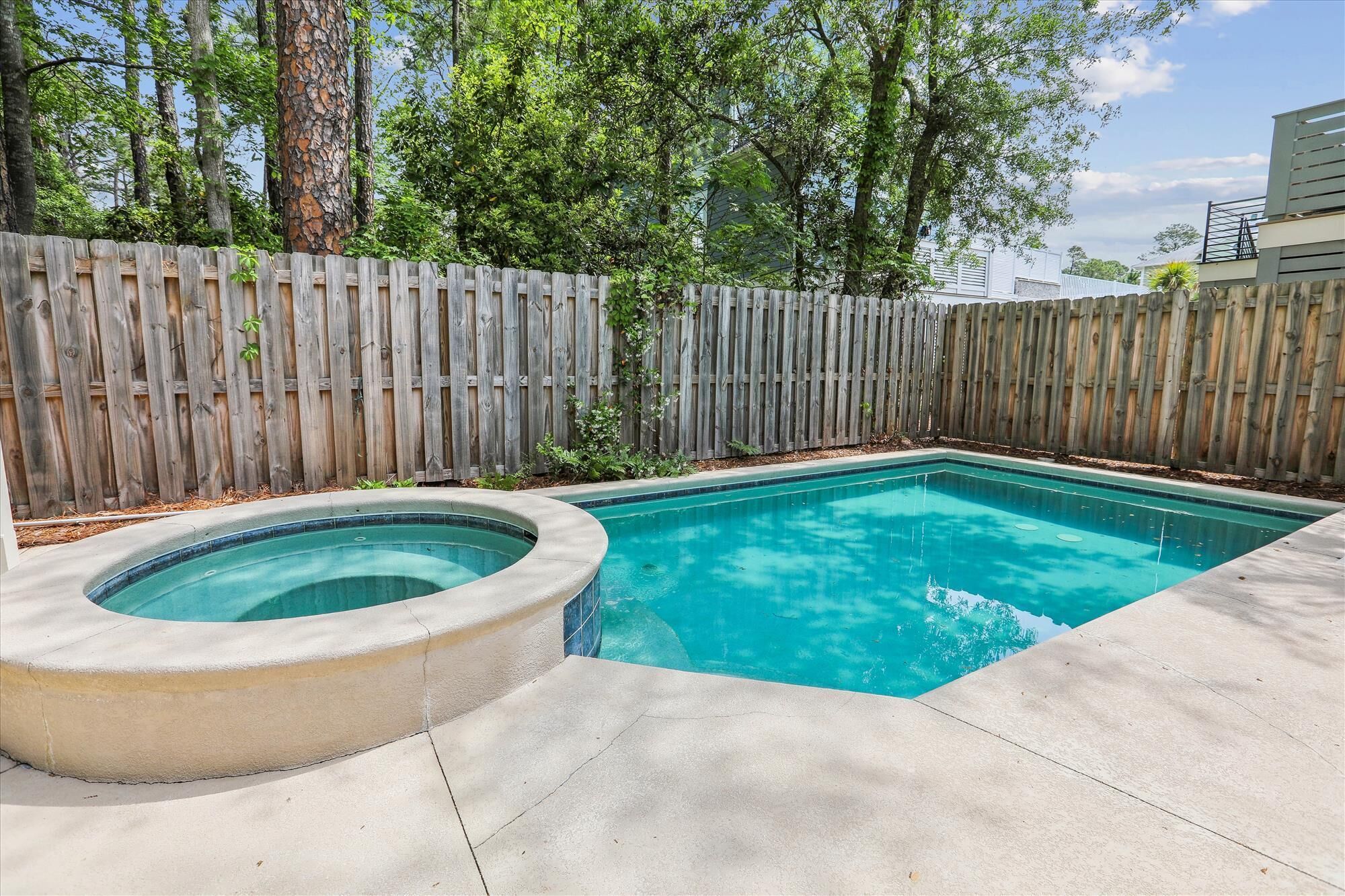 Una piscina con valla de madera y árboles al fondo.