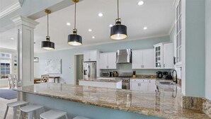Una cocina moderna con armarios blancos, encimera de granito e iluminación colgante.